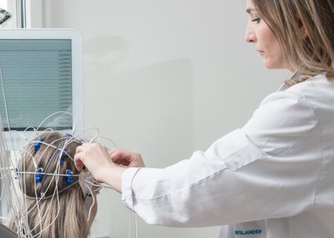Eine Mitarbeiterin befestigt EEG-Elektroden am Kopf einer Patientin.