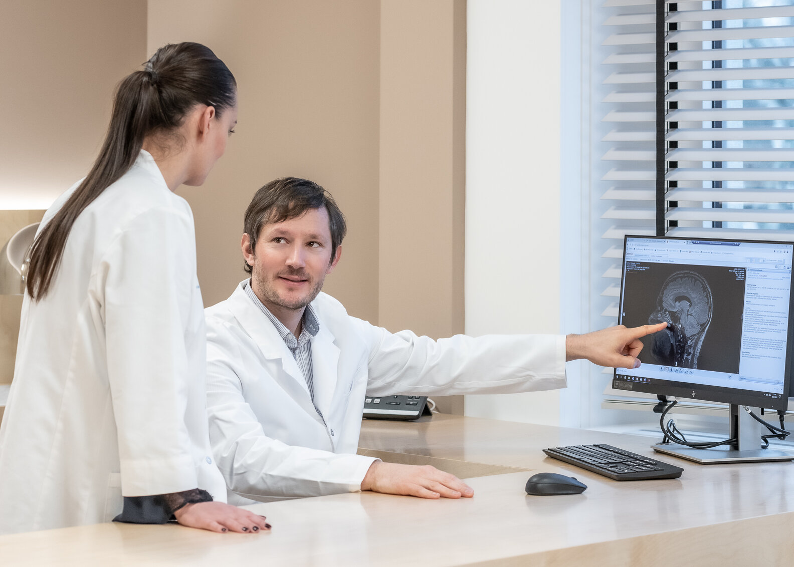 Der Neurologe, Dr. Nikolai Pfender zeigt einer Mitarbeiterin etwas auf seinem Bildschirm.