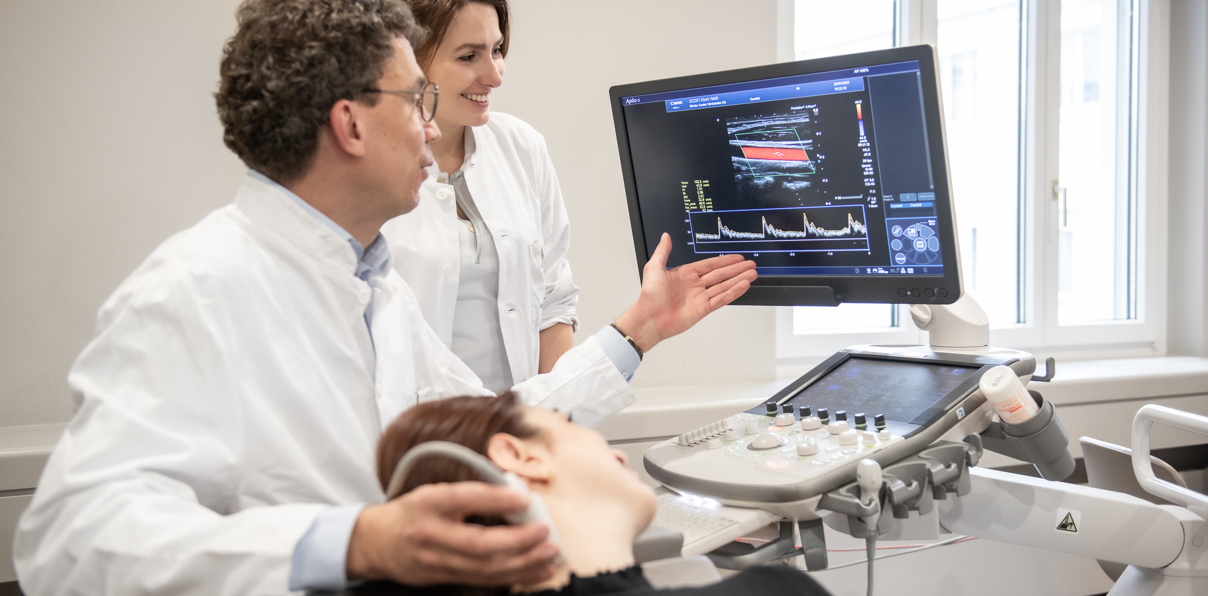 Schlaganfall Ambulatorium - Neurologe führt eine Doppler Untersuchung durch und zeigt die Ergebnisse auf einem Bildschirm.