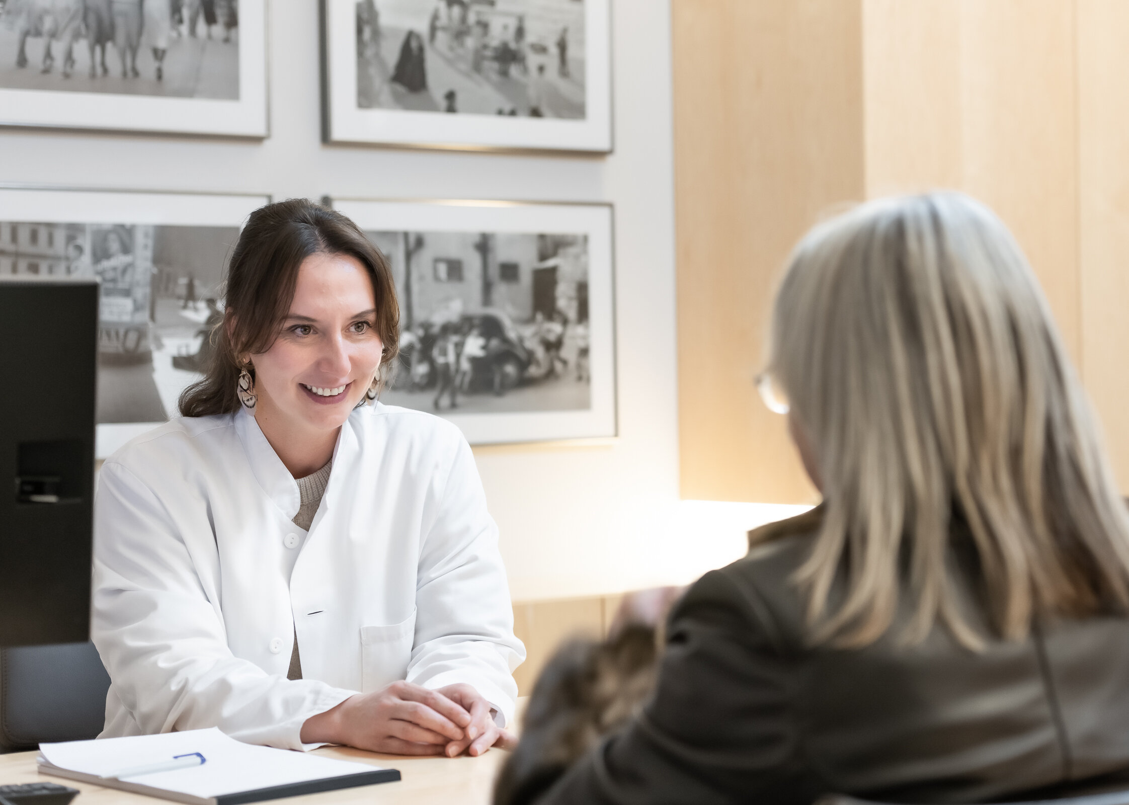 Die Neurologin, Bettina Anders sitzt an ihrem Schreibtisch und spricht mit einer Patientin.